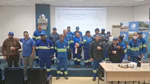 Funcionários da equipe de manutenção (vestidos em uniformes azuis) aparecem reunidos após o treinamento de roçada e capina